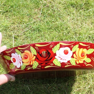 May include: A red, round, wooden bowl with a floral design painted on the rim. The design features pink, yellow, and red roses with green leaves.