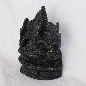 May include: Black stone sculpture of the Hindu deity Ganesha, sitting on a lotus throne. The sculpture is intricately carved with details on the elephant head, trunk, and body.