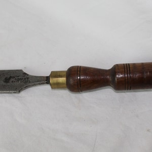 Op de afbeelding: Een vintage beitel met een houten handvat, een messing bus en een stalen blad met de tekst "Stanley Easy Steel".