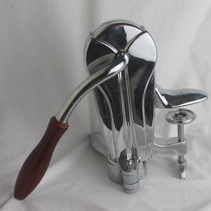 Può includere: Un apribottiglie in cromo e legno con una maniglia a leva e un morsetto per tenere la bottiglia.