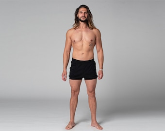 May include: A person wearing black athletic shorts. The shorts are above the knee and have a drawstring. The person is standing in front of a gray background.