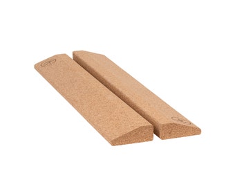 May include: Two rectangular cork yoga blocks with a beveled edge. The blocks are light brown and have a textured surface. A small logo is printed on the top of each block.