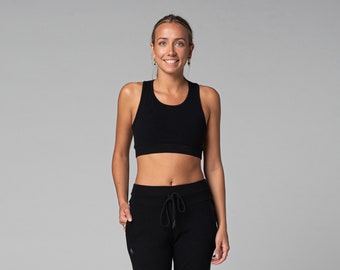 Könnte beinhalten: Eine Frau trägt einen schwarzen Sport-BH und eine schwarze Jogginghose mit Kordelzug. Die Sportbekleidung ist aus einem strukturierten Stoff gefertigt. Der Hintergrund ist einfarbig hellgrau.