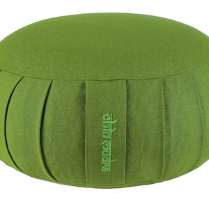 May include: A round, green meditation cushion with a pleated design around the sides. The cushion has a flat top and bottom and a small green embroidered logo on the side. The cushion is made of a textured fabric.
