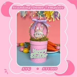 May include: A pink standing dome template with a bunny cutout inside the dome. The dome is topped with a purple ribbon and the base of the dome is decorated with a green Happy Easter cutout.