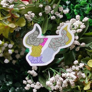 May include: A white sticker with a green, pink, and yellow succulent design. The sticker is shaped like a bull's head.