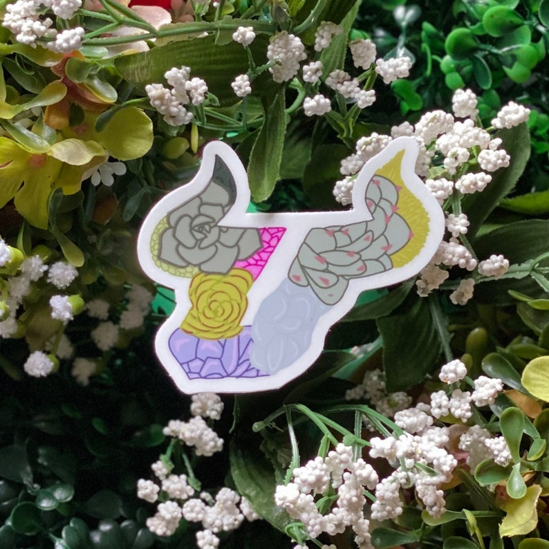 May include: A white sticker with a green, pink, and yellow succulent design. The sticker is shaped like a bull's head.