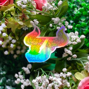 May include: A holographic sticker of a rainbow-colored floral design. The sticker is shaped like a stylized number seven.