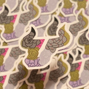 May include: A sticker featuring a stylized bull's head with a floral design. The bull's head is outlined in black and filled with a variety of succulents in shades of green, pink, and purple.