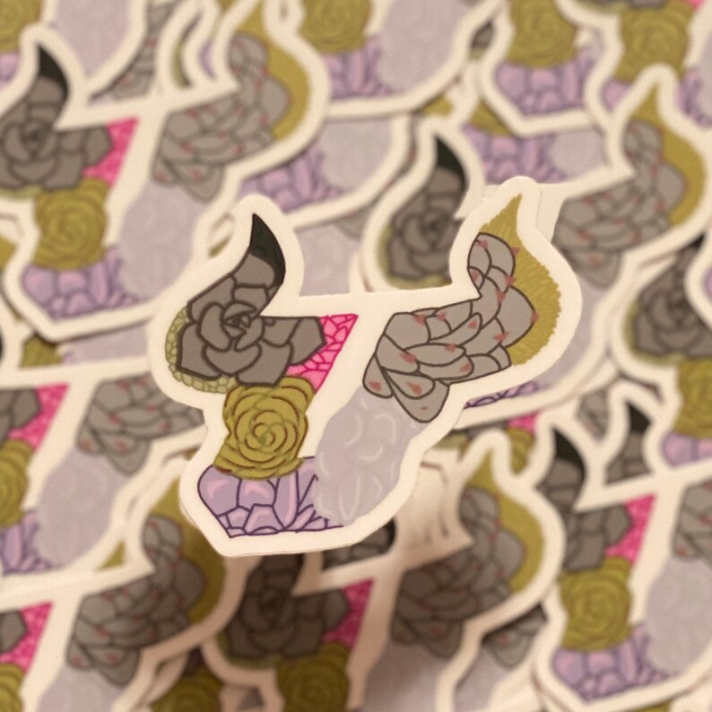 May include: A sticker featuring a stylized bull's head with a floral design. The bull's head is outlined in black and filled with a variety of succulents in shades of green, pink, and purple.