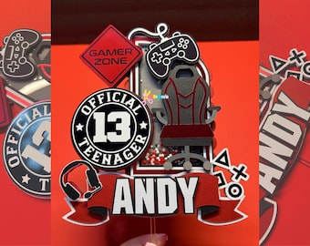 May include: A red, black, and white cake topper with the text "Official Teenager 13" and "Andy". The topper also features a gaming chair, a video game controller, and a headset.