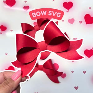 May include: Red paper bow with a white outline, against a background of pink hearts. The text "BOW SVG" is in a white box with a pink outline.