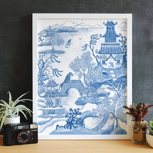 May include: A framed blue and white watercolor print featuring an Asian-inspired landscape with pagodas, trees, and tigers. The artwork is in a white frame and is displayed on a wooden surface.