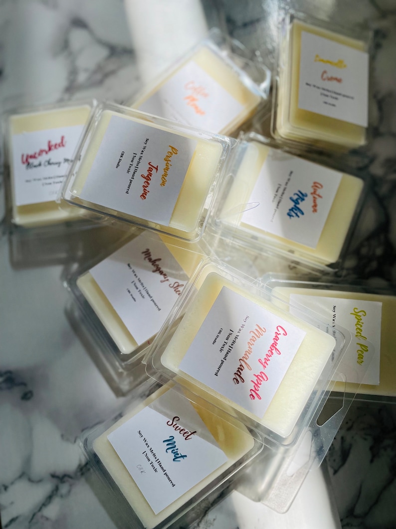 May include: Assortment of soy wax melts in clear plastic containers. The scents include Spiced Pear, Cranberry Apple Marmalade, Mahogany Shea, Persimmon Tangerine, Sweet Mint, and Uncorked Black Cherry Merlot. Each container has a label with the scent name and the text "Soy Wax Melts Hand Poured, Non Toxic".