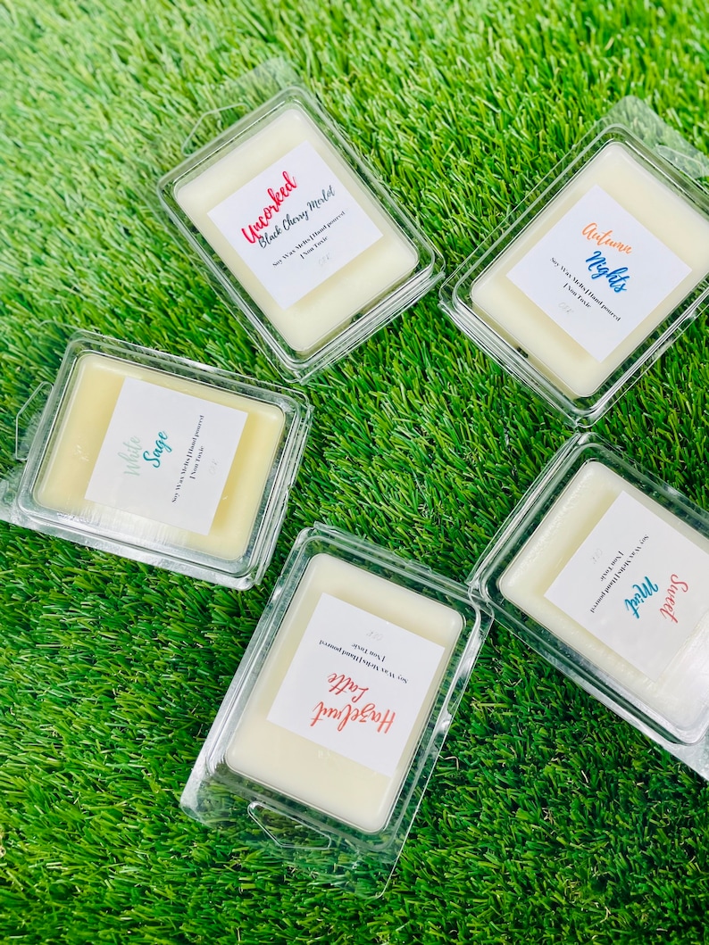 May include: Five clear plastic containers with wax melts inside. The wax melts are labeled with different scents: "Uncorked Black Cherry Merlot", "Autumn Nights", "White Sage", "Hazelnut Latte", and "Sweet & Proud".