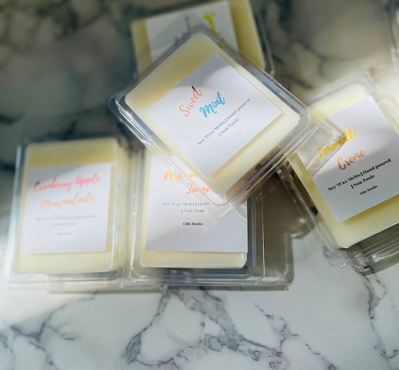 May include: A collection of six soy wax melts in clear plastic containers. The wax melts are hand-poured and non-toxic. The scents include Cranberry Apple Marmalade, Sweet Mint, Pear Jam, Lemonade Creme.