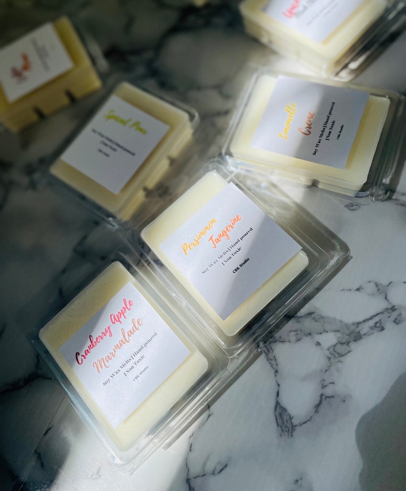 May include: Assortment of soy wax melts in clear plastic containers. The wax melts are hand-poured and come in a variety of scents, including Cranberry Apple Marmalade, Persimmon Tangerine, and Creme. Each melt is labeled with the scent and the words "Soy Wax Melts Hand Poured" and "Non Toxic".
