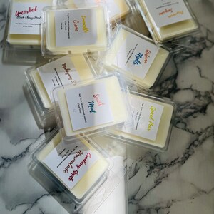 May include: A collection of wax melts in clear plastic containers with labels. The labels have different scents, including Cranberry Apple, Mahogany & Spice, Sweet Mint, Spiced Pear, Limoncello Creme, Autumn Nights, and Tangerine.
