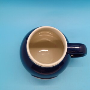Pu&ograve; includere: Una tazza in ceramica blu scuro con un bordo bianco. La tazza ha una forma arrotondata e un manico.