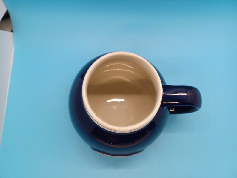 Pu&ograve; includere: Una tazza in ceramica blu scuro con un bordo bianco. La tazza ha una forma arrotondata e un manico.