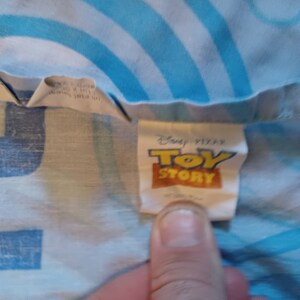May include: A white tag with blue text that reads "Disney Pixar Toy Story" on a blue and white patterned fabric.