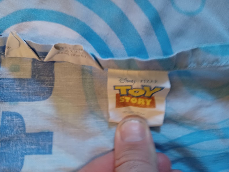 May include: A white tag with blue text that reads "Disney Pixar Toy Story" on a blue and white patterned fabric.