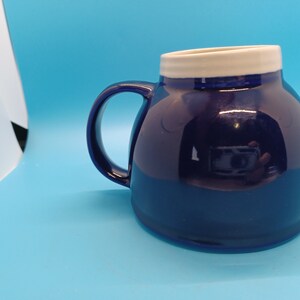 Pu&ograve; includere: Una tazza in ceramica blu scuro con un bordo bianco. La tazza ha una forma arrotondata e un manico.