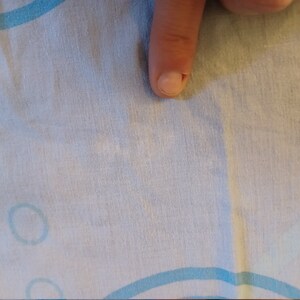 May include: A close-up of a white fabric with a light blue pattern of circles. The fabric has a slight wrinkle in the center.
