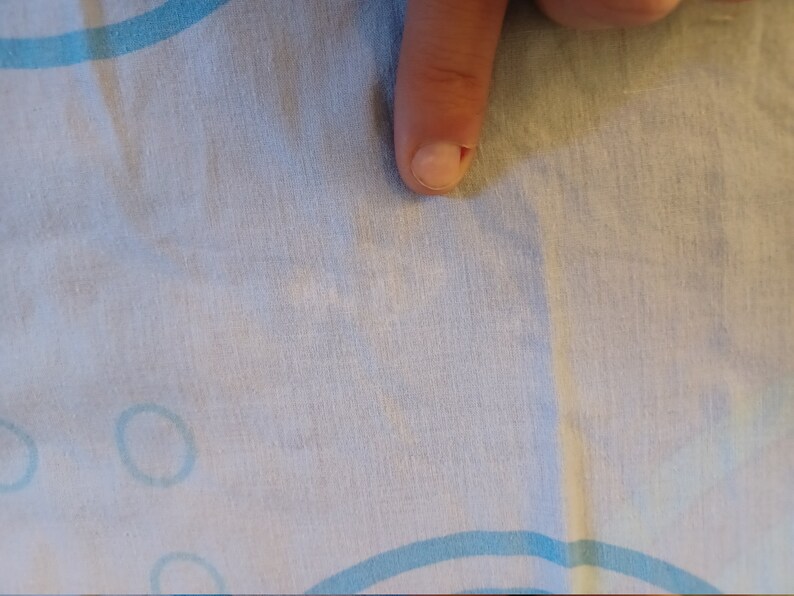 May include: A close-up of a white fabric with a light blue pattern of circles. The fabric has a slight wrinkle in the center.