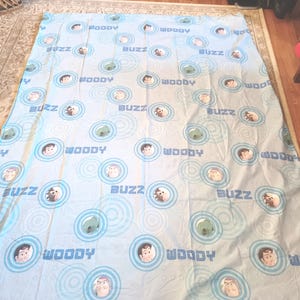 May include: A blue and white twin-sized bed sheet with a repeating pattern of Woody and Buzz Lightyear from the Toy Story movie franchise. The characters are surrounded by blue and white concentric circles.