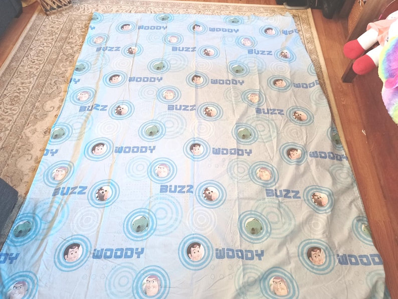 May include: A blue and white twin-sized bed sheet with a repeating pattern of Woody and Buzz Lightyear from the Toy Story movie franchise. The characters are surrounded by blue and white concentric circles.