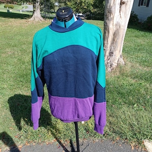 May include: A teal, navy blue, and purple color block sweatshirt with long sleeves.