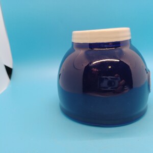 Pu&ograve; includere: Un vaso di ceramica blu scuro con un coperchio bianco. Il vaso ha una finitura liscia e lucida.