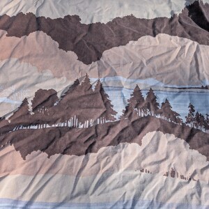 Puede incluir: Una tela con un diseño de paisaje de montañas y bosques. El patrón presenta tonos marrones, beige y azules, con árboles estilizados y siluetas de montañas. La tela tiene una textura arrugada.
