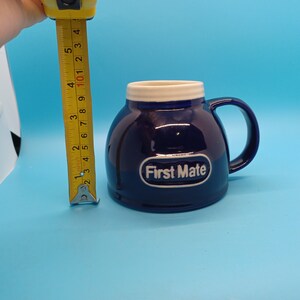 Pu&ograve; includere: Una tazza in ceramica blu con un bordo e un manico bianchi. La tazza ha un logo ovale bianco che dice "First Mate".