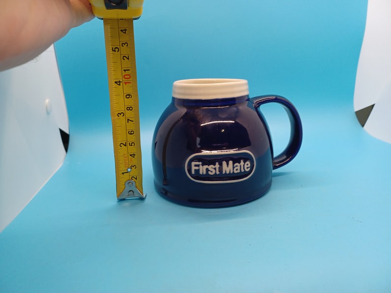 Pu&ograve; includere: Una tazza in ceramica blu con un bordo e un manico bianchi. La tazza ha un logo ovale bianco che dice "First Mate".
