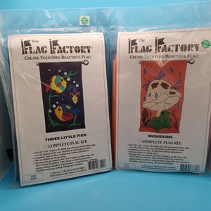 May include: Two packages of The Flag Factory complete flag kits. The left package features a blue background with three colorful fish and the text "Three Little Fish". The right package features a red background with a mushroom and a frog and the text "Mushrooms".