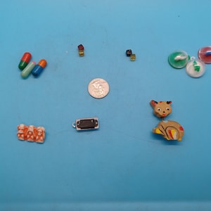 May include: Assortment of small toys and trinkets including a wooden deer figurine, a small harmonica, a silver coin, three plastic capsules, two small plastic blocks, and two plastic spinning tops.