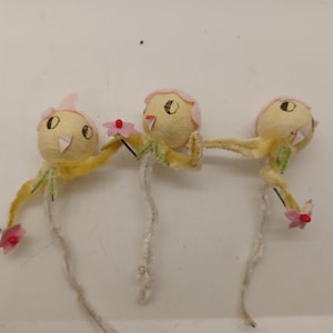 May include: Three yellow felt bird ornaments with pink felt hats and flowers. The birds have black eyes and a white beak. The flowers are pink with red centers.