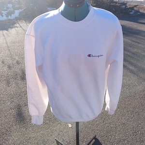 May include: White long-sleeve Champion sweatshirt with a small blue and red Champion logo on the front.