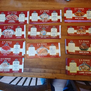 May include: A collection of vintage S.S. Pierce food product boxes, featuring various dishes like Chicken Cacciatore, Beef Stew, and Spaghetti. The boxes are red with white and gold accents, showcasing the brand's logo and product images.