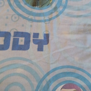 May include: A blue and white fabric with the word "Buddy" printed on it. The fabric has a pattern of blue circles.
