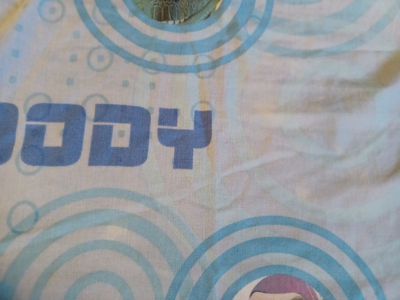 May include: A blue and white fabric with the word "Buddy" printed on it. The fabric has a pattern of blue circles.