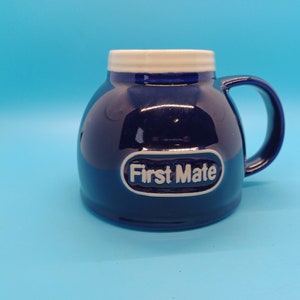 Pu&ograve; includere: Una tazza in ceramica blu con un bordo e un manico bianchi. La tazza ha un ovale bianco con il testo "First Mate" in lettere nere.
