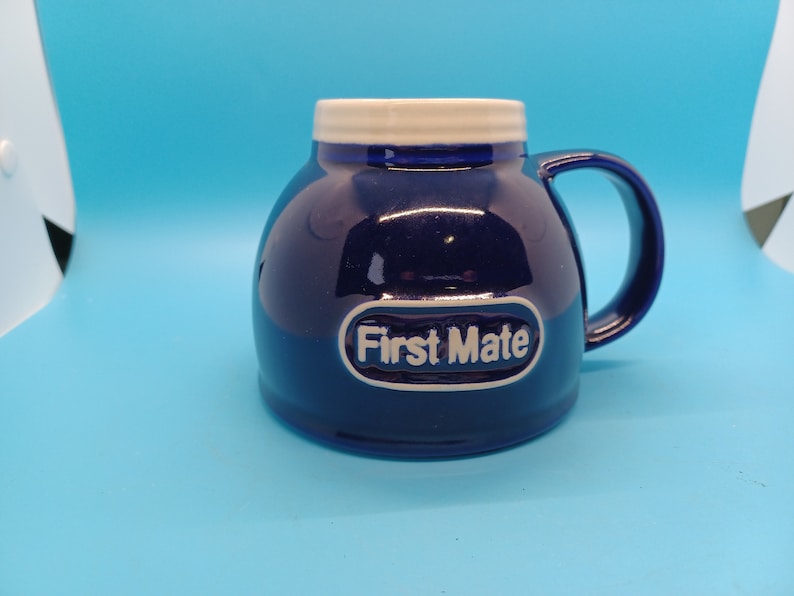 Pu&ograve; includere: Una tazza in ceramica blu con un bordo e un manico bianchi. La tazza ha un ovale bianco con il testo "First Mate" in lettere nere.