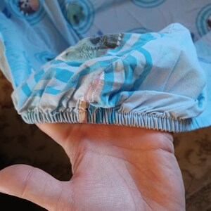 May include: Close-up of a blue and white fitted sheet with a colorful pattern. The sheet has a gathered elastic edge.