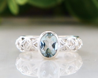 May include: A silver ring with an oval-shaped blue gemstone set in a delicate, intricate design.
