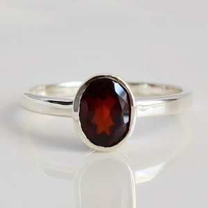 Könnte beinhalten: Ein silberner Ring mit einem roten ovalen Edelstein.