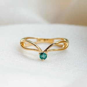 Könnte beinhalten: Ein goldener Ring mit einem zarten, geschwungenen Design und einem einzigen, runden, grünen Edelstein in der Mitte.