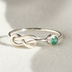 May include: A silver ring with a knot design and a small green gemstone.